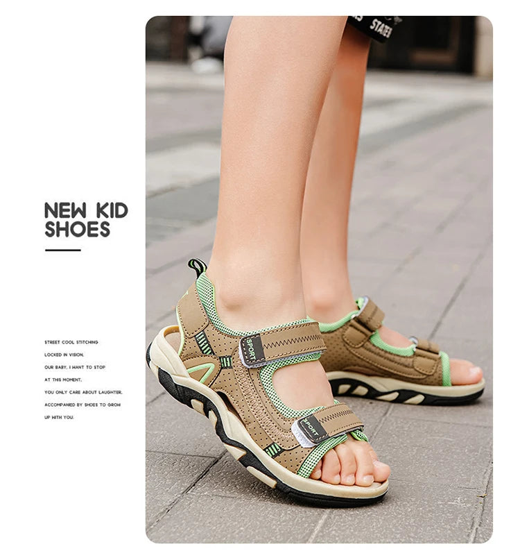A close-up of a pair of tan and green breathable summer sport sandals for kids being worn on a sidewalk.
