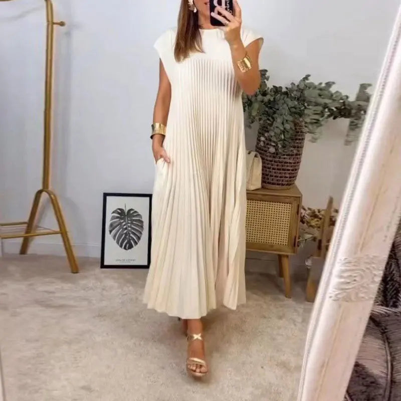 A woman wearing a cream pleated midi dress with a round neck standing indoors.