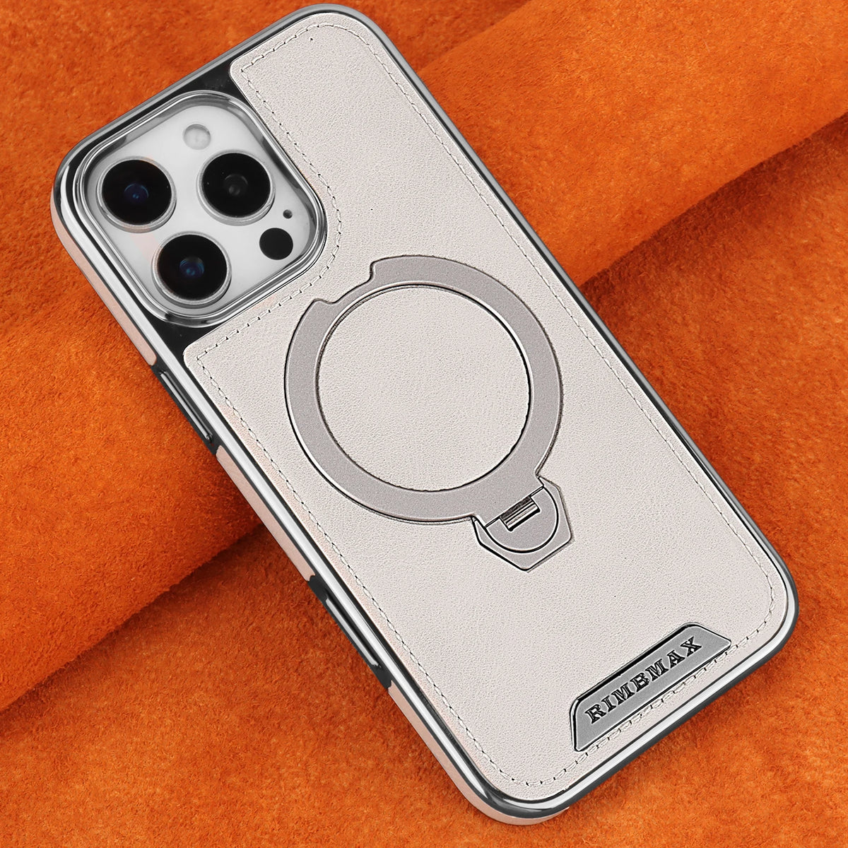 A silver iPhone case with a leather finish and a rotating magnetic stand is placed on an orange fabric.