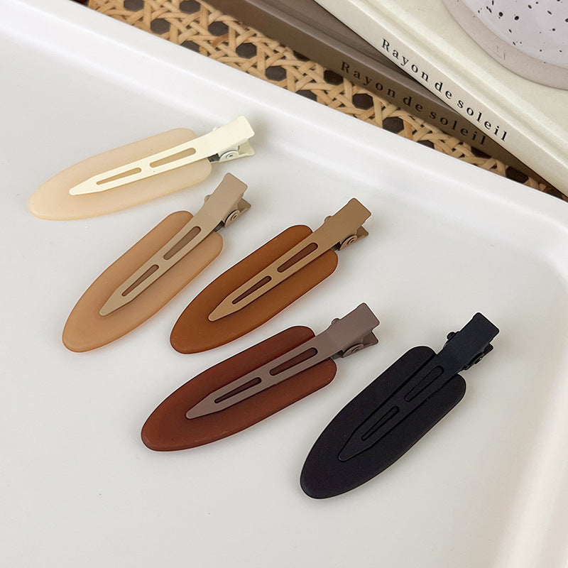 A set of two matte resin side hair clips in various earth tones, including beige, tan, and black.