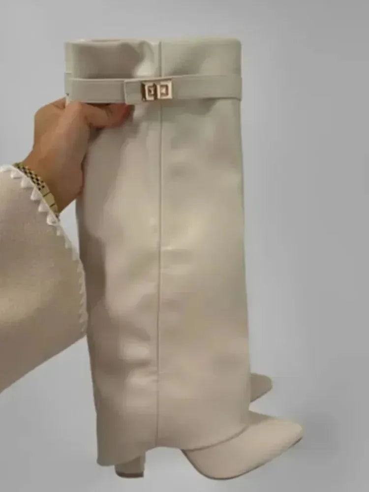 A close-up of a beige knee-high boot with a fabric strap and metal buckle being held by a hand.