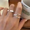 En hånd med tre sølvjusterbare ringe på en finger ved siden af en hvid keramisk kop.