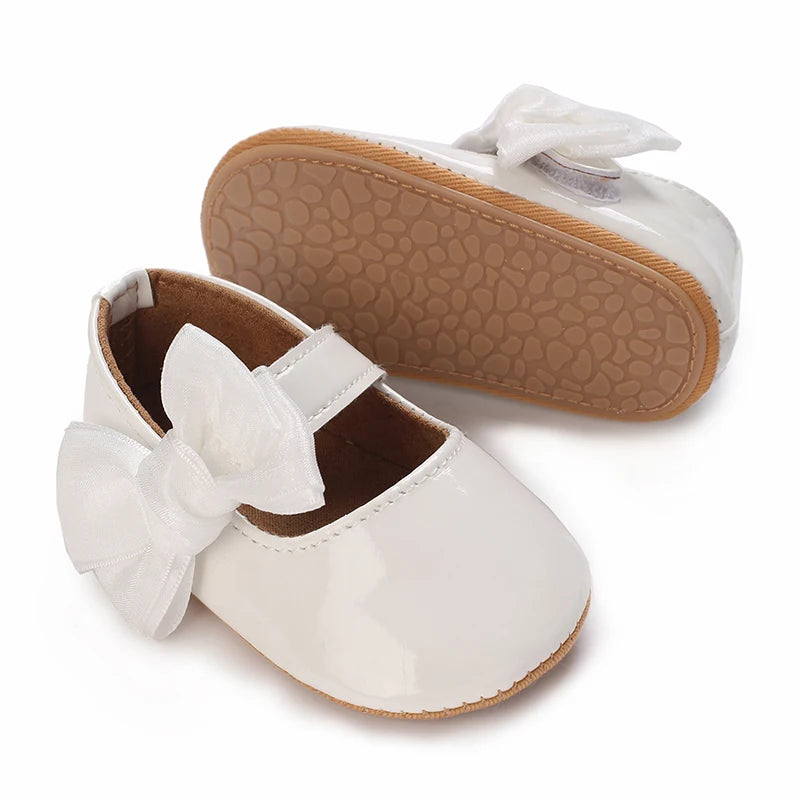 A pair of white baby first walker shoes with a light brown sole and bow detail.