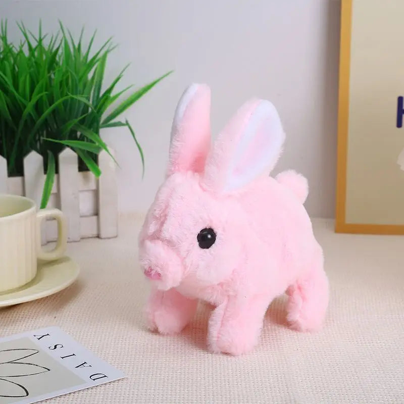 A pink bunny plush toy with long ears is shown on a white surface next to a potted plant.