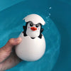 A white bath toy shaped like a penguin with an orange beak is being held over blue water.