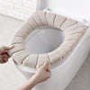 A hand is placing a beige, textured acrylic toilet seat cover onto a white toilet bowl.