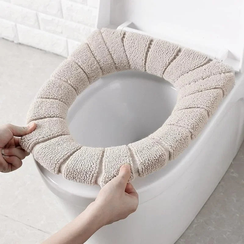 A hand is placing a beige, textured acrylic toilet seat cover onto a white toilet bowl.