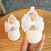 A pair of white lace baby first walker shoes with bows resting on a wooden surface.