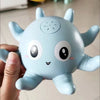 A light blue musical whale bath toy with large eyes and a smiling mouth is held in a hand.