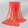 A vibrant orange gold shimmer chiffon scarf and head wrap displayed on a hanger.