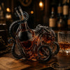 Mørk ravfarget glassblekksprutwhiskydekanter på treflate ved siden av en gammel nøkkel.
