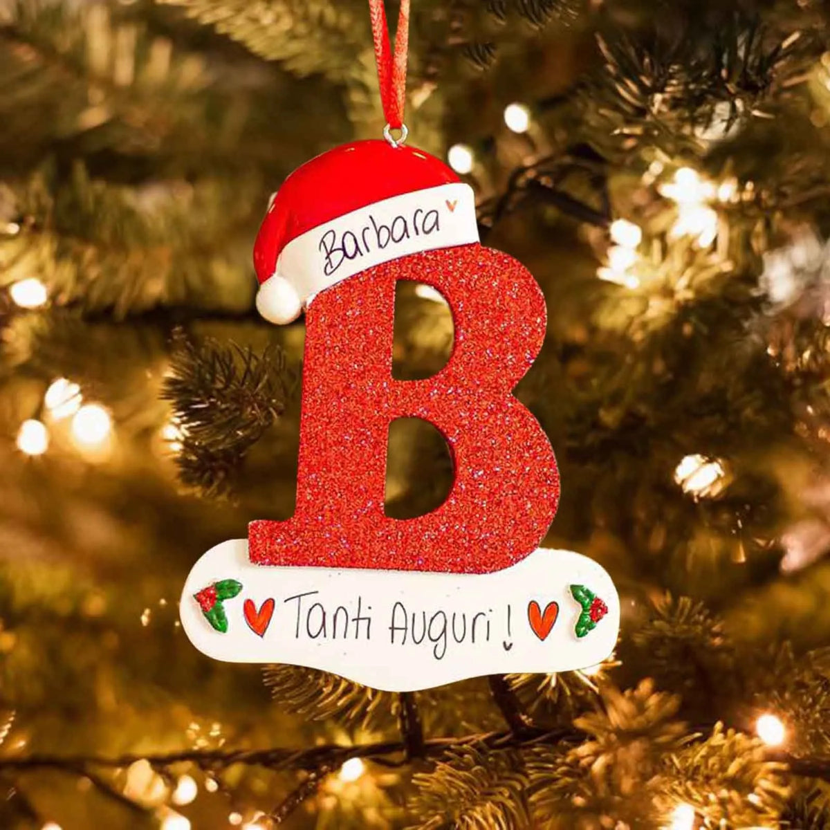 Rød julenisse-akrylpynt i form av bokstaven B med glitter, hengende på juletre.