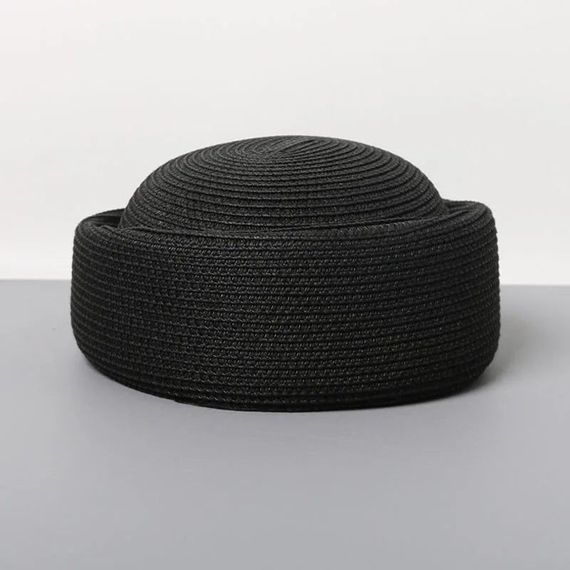 A black woven straw pillbox sun hat with a wide brim shown against a light gray background.