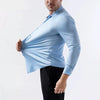 Hombre con camisa azul claro sin planchar y pantalones negros, de pecho hacia arriba.