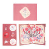 A pink card featuring a floral design and a couple silhouette on the front, with accompanying circular elements.