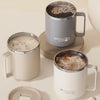 A set of two beige double wall insulated stainless steel travel mugs, one filled with coffee and the other empty.