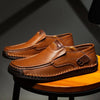 Et par brune håndlavede ægte læderslip-on loafers til mænd, hvilende på en træoverflade.