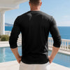 A man wearing a black long-sleeve shirt standing outdoors near a pool and ocean view.