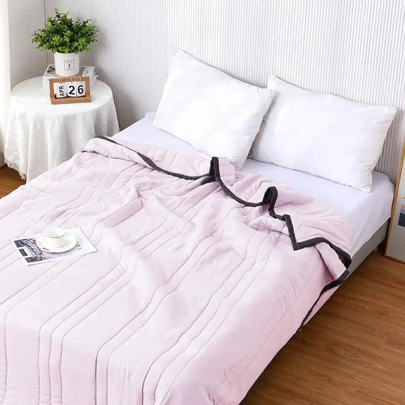 A pink quilted throw blanket is displayed on a bed with white pillows and a potted plant in the background.