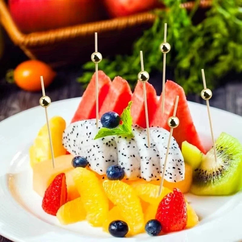 Colorful fruit skewers featuring strawberries, kiwi, orange segments, and white melon pieces on a white plate.