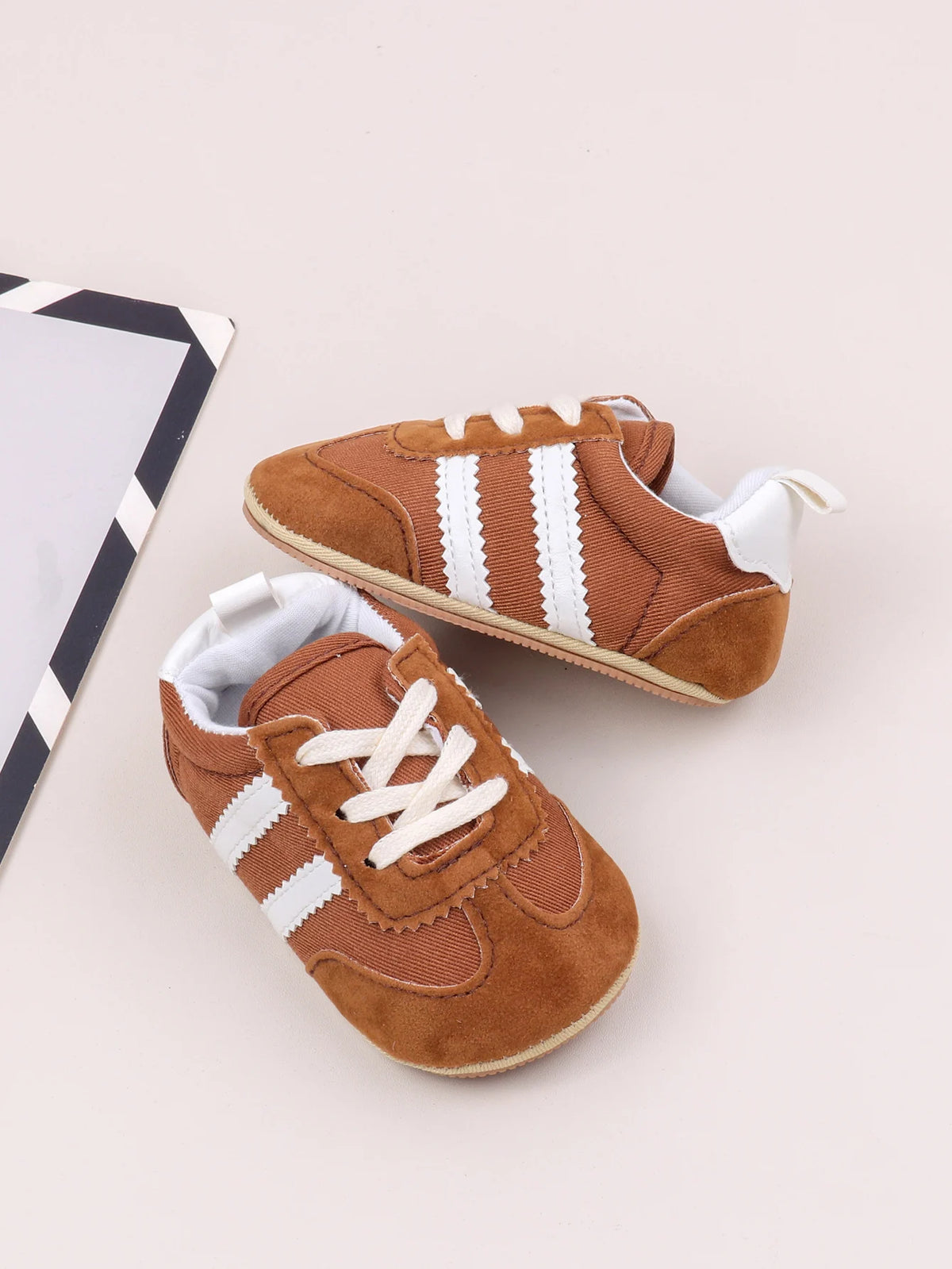 A pair of brown and white striped baby first walker shoes with canvas upper and anti-slip sole