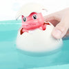A hand is holding a bath toy shaped like a pink duck or penguin that sprays water into a blue tub.