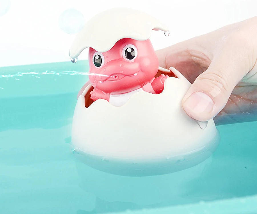 A hand is holding a bath toy shaped like a pink duck or penguin that sprays water into a blue tub.