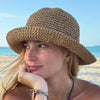 A woman wearing a wide-brimmed crochet straw fisherman hat outdoors by the sea.