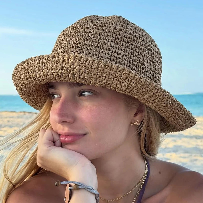 A woman wearing a wide-brimmed crochet straw fisherman hat outdoors by the sea.
