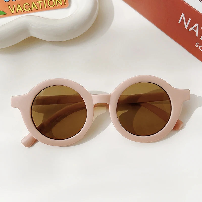 A pair of light pink sunglasses with brown tinted lenses resting on a white surface.