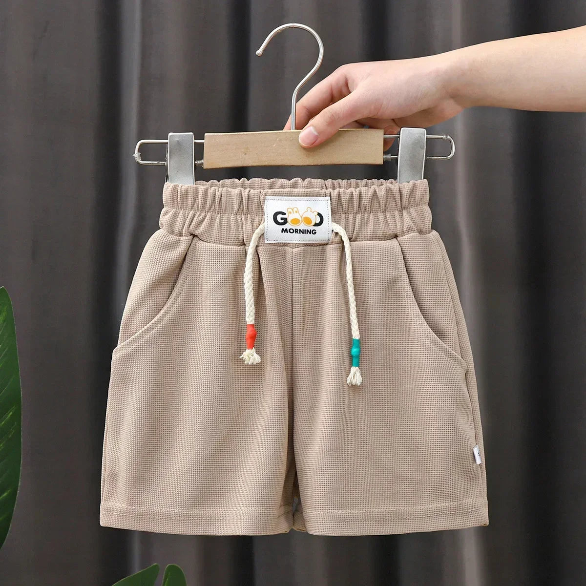 Tan kids beach shorts with elastic waist hanging on a clothes hanger