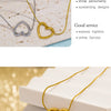A close-up of a dainty gold heart pendant necklace with a snake chain displayed on a light background.
