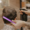 Manos usan un peine morado para desenredar y peinar el cabello de una persona.