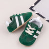 A pair of green and white baby first walker shoes with a textured sole are shown on a light background.