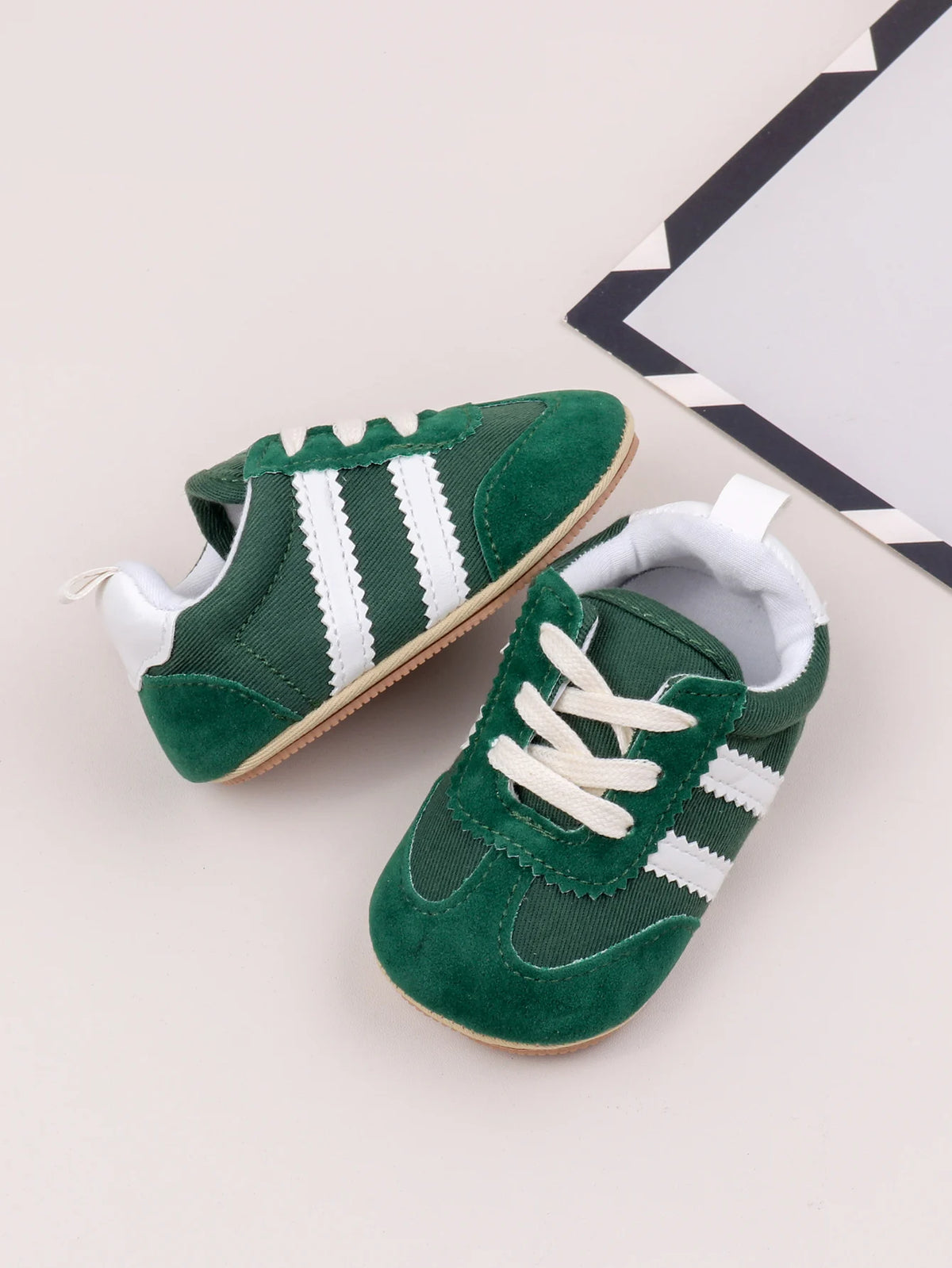 A pair of green and white baby first walker shoes with a textured sole are shown on a light background.