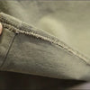 A hand is pulling the hem of a khaki green cotton shirt and cargo pants set to show the stitching detail.