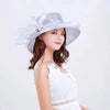 A woman wearing a light gray wide brim organza sun hat with ruffled mesh and a white lace top.