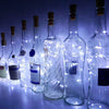 A row of glass bottles filled with LED fairy lights, illuminated against a dark blue background.