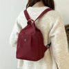 A maroon lightweight oxford cloth mini backpack worn by a woman in a cream sweater.