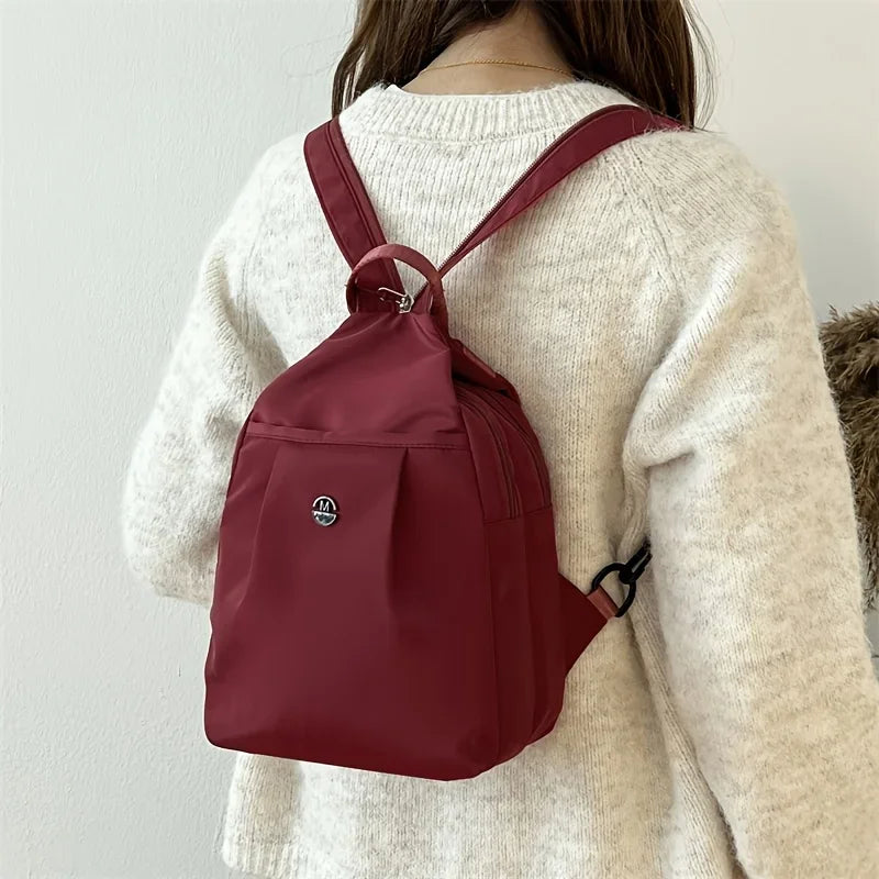 A maroon lightweight oxford cloth mini backpack worn by a woman in a cream sweater.