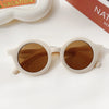 A pair of light-colored sunglasses with brown lenses resting on a white surface.