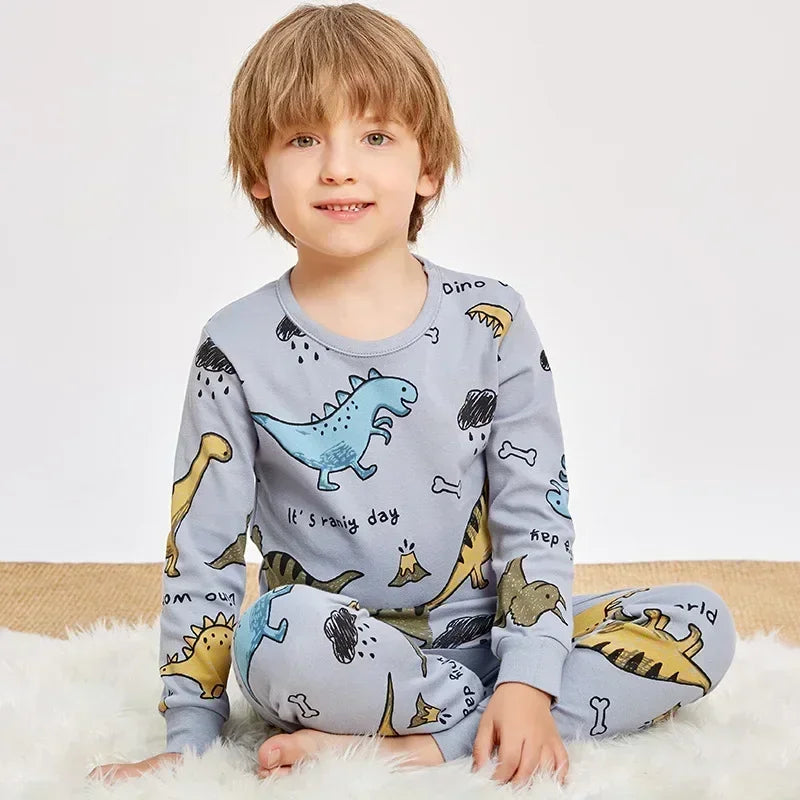 A young boy wearing a light blue dinosaur-themed long-sleeved pajama set