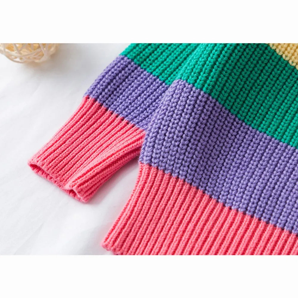 A close-up of a girls' rainbow striped knit sweater featuring vibrant pink, purple, and green horizontal stripes.