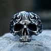 A detailed gothic carved skull ring made of 316L stainless steel resting on a gray surface.