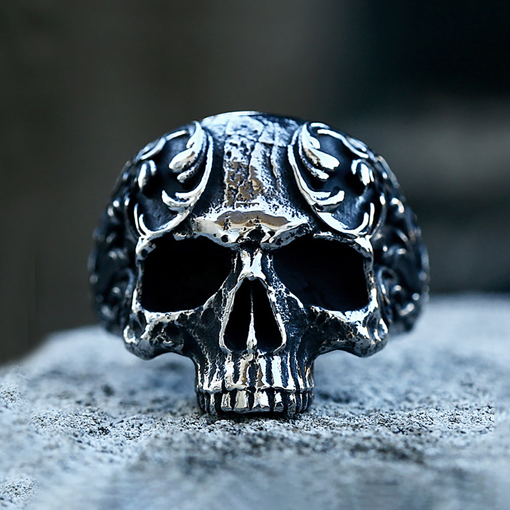 A detailed gothic carved skull ring made of 316L stainless steel resting on a gray surface.