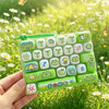 A hand holds a green silicone keychain featuring a keyboard design with cartoon animals and symbols.