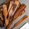 A set of natural teak wood cooking utensils, including spatulas and spoons, resting on a wooden cutting board.