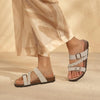A close-up of women's cork footbed slide sandals with white braided straps and brown sole against a neutral background.