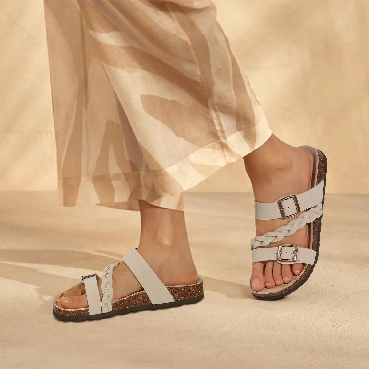 A close-up of women's cork footbed slide sandals with white braided straps and brown sole against a neutral background.