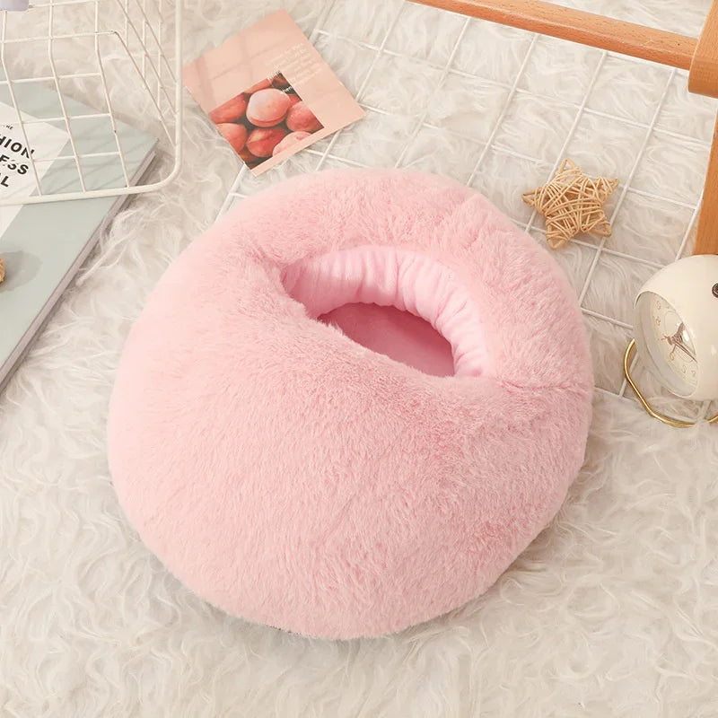 A pink, fluffy USB heated foot warmer with a soft fleece cover resting on a white textured surface.